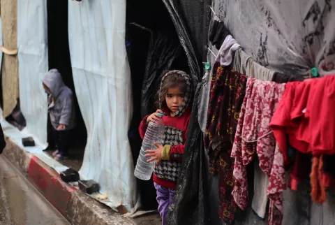 Par une journée pluvieuse, une jeune fille se tient devant son abri à Rafah, une bouteille d'eau vide à la main.